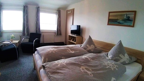 A hotel room with two beds, a desk, a chair, a TV, and a painting on the wall. - Room 4 - Pension Restaurant Zur Brücke (Wittmund)