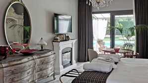 A hotel room with a bed, a fireplace, a television, a dining table with chairs, and a view of a swimming pool. - Exclusive Villa with Private Pool Sleeps 12 - 6 Rooms (Castelbaldo)