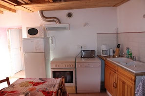 Cocina compacta con refrigerador, microondas, horno y lavavajillas. Hay una mesa de madera con sillas, un lavabo y una ventana.