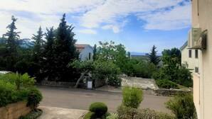 A residential area with a paved courtyard, surrounded by trees and a building with a red-tiled roof. - En-suite room Helena nr. 1 in town Krk with air conditioning, WiFi, parking (Krk)