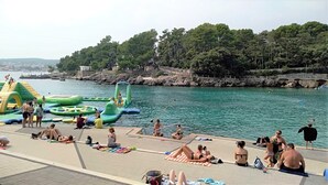 A waterfront area with inflatable water toys and people relaxing on the shore. - En-suite room Helena nr. 1 in town Krk with air conditioning, WiFi, parking (Krk)