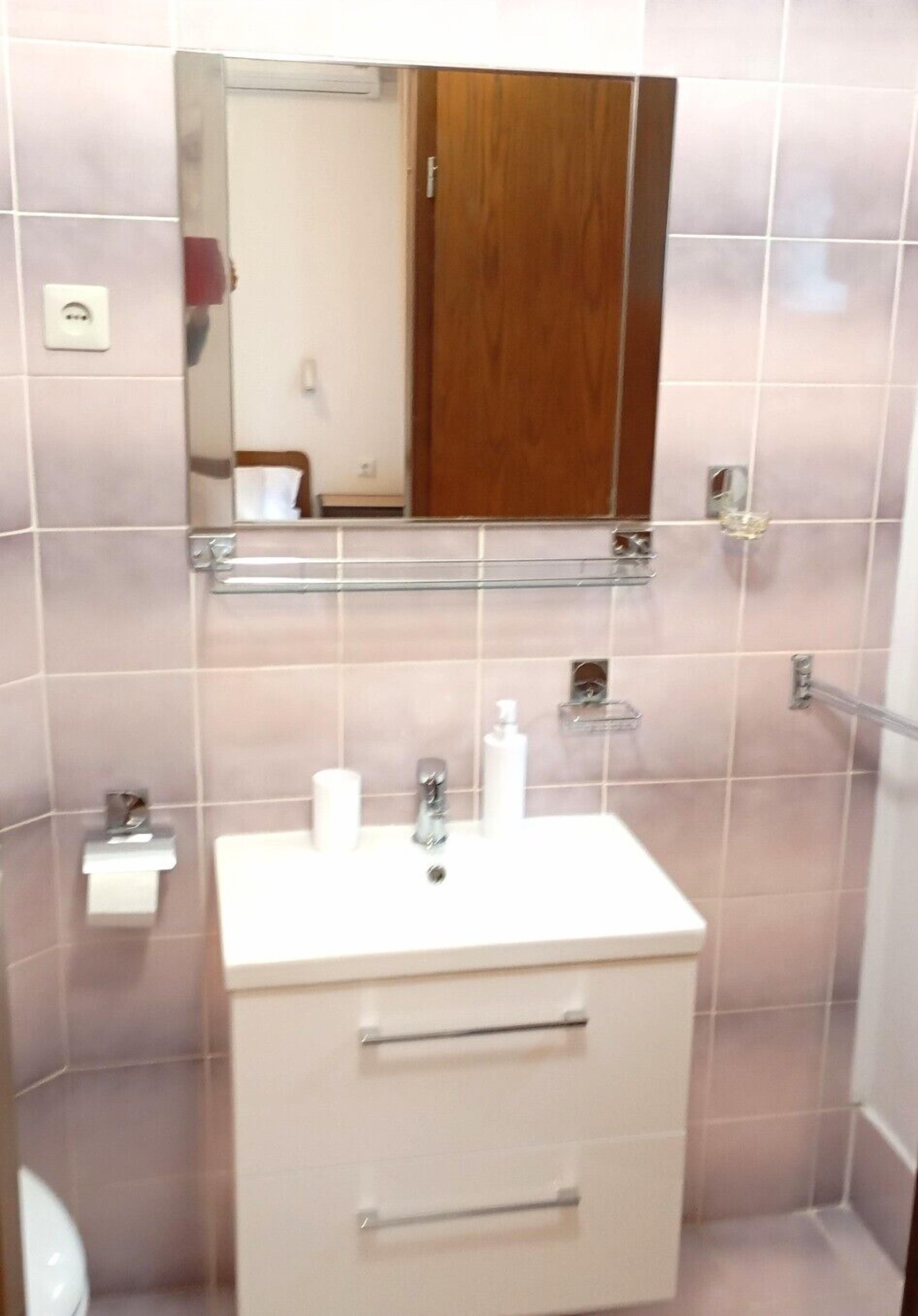 A bathroom with a white sink, mirror, and wooden cabinet.