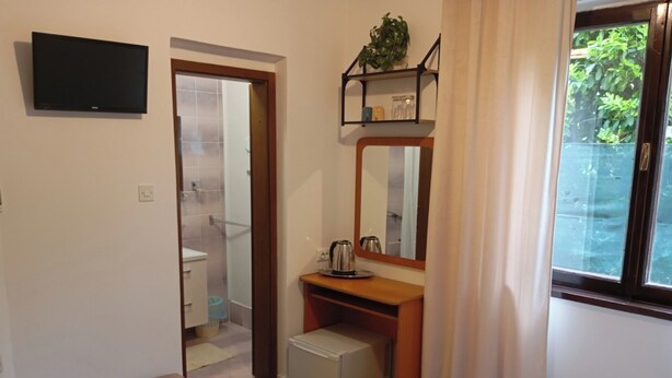 A bedroom with a bed, a bedside table, a mirror, a TV mounted on the wall, and a window with a view of greenery. - En-suite room Helena nr. 1 in town Krk with air conditioning, WiFi, parking (Krk)