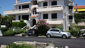 A two-story building with a balcony on the second floor, a staircase leading to the entrance, and a car parked in front. - En-suite room Helena nr. 1 in town Krk with air conditioning, WiFi, parking (Krk)