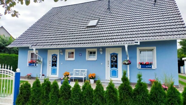 A blue house with a tiled roof, a white fence, and a bench outside. - Friesenhus - Ferienwohnung (Kühlungsborn)