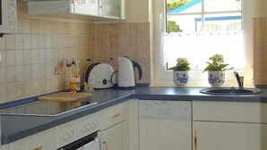 A kitchen with a built-in dishwasher, a stove, and a window with a view of a house. - Friesenhus - Ferienwohnung (Kühlungsborn)