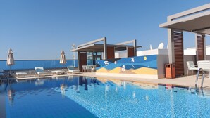 A swimming pool with lounge chairs and umbrellas, a mural with space-themed artwork, and a clear blue sky. - Beach Walk Hotel (Dubai)