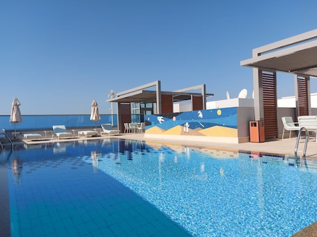 Una piscina al aire libre, sombrillas, sillones reclinables de piscina