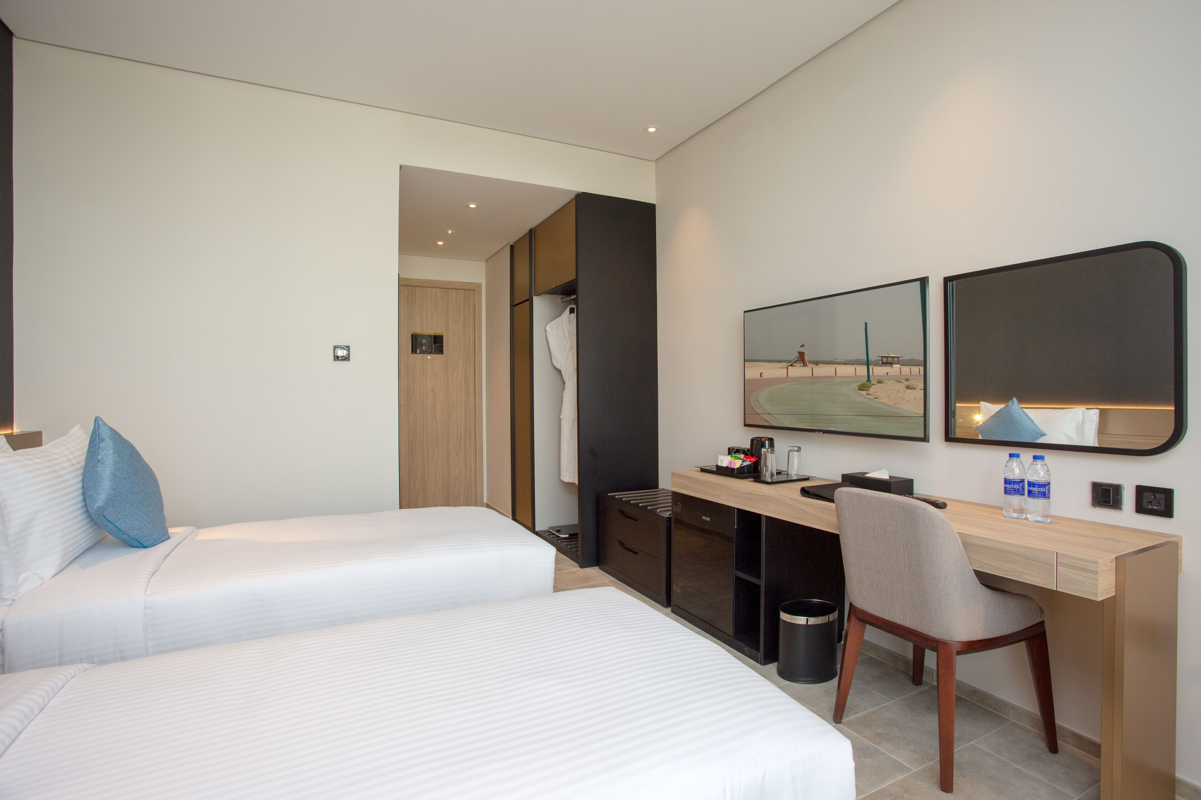 A hotel room with two beds, a desk, a chair, a mirror, and a trash can.