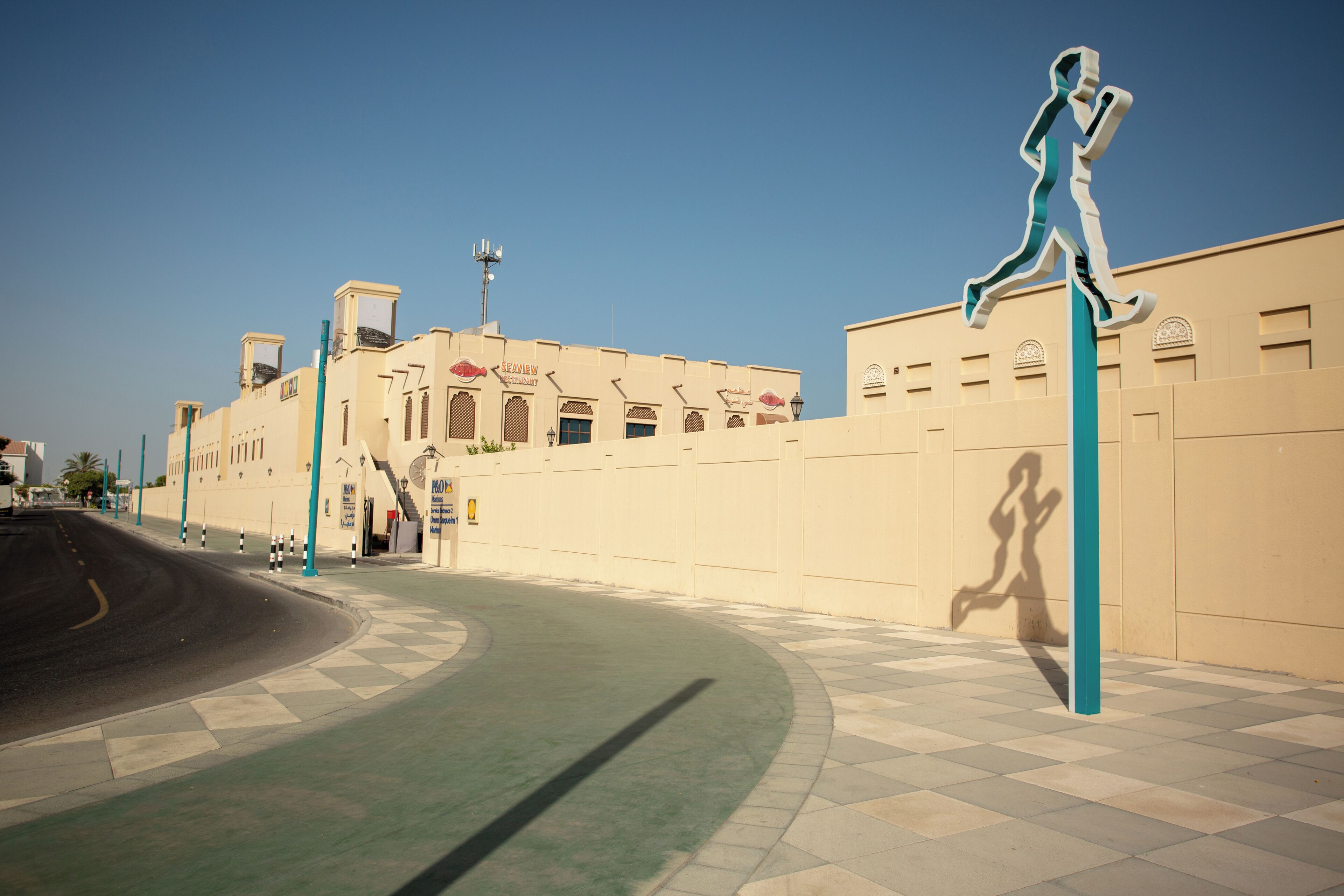 A curved pathway leading to a building with a checkered floor pattern and a large sculpture of a running figure.