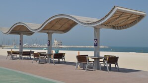 A beachside seating area with curved canopies and tables, overlooking a sandy beach and the sea. - Beach Walk Hotel (Dubai)