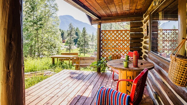 Een houten terras met een tafel en stoelen, met uitzicht op een bos en bergen.