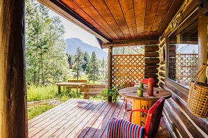 A wooden deck with a table and chairs, overlooking a forest and mountains. - Authentic Vintage Cabin 9 Miles from Glacier (Martin City)