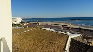 A beach view with a white building, a sandy area, and a clear blue sky.