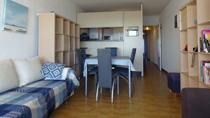 A compact living space with a dining area, kitchenette, and a bookshelf.