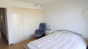 A bedroom with a bed, a chair, a desk, and a wardrobe.