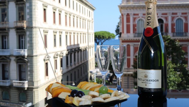 A bottle of Moët & Chandon champagne, two glasses, and a fruit platter on a table with a cityscape in the background. - Suite Napoli Riviera (Naples)
