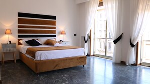 A modern bedroom with a large bed, two bedside lamps, a decorative wall panel, and a view through a large window with curtains. - Suite Napoli Riviera (Naples)