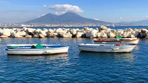 A harbor with boats docked near a rocky breakwater, a mountain in the background, and a clear sky. - Suite Napoli Riviera (Naples)