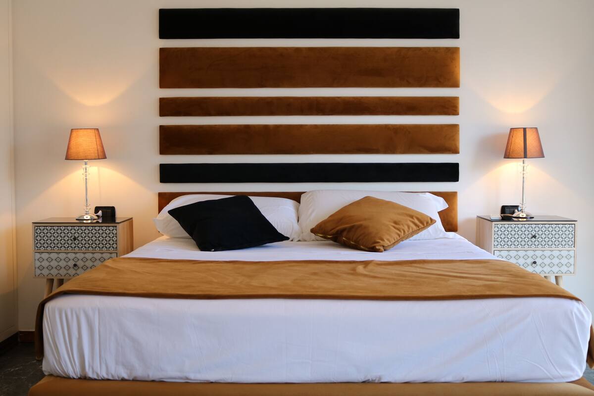 A neatly made bed with white and brown bedding, flanked by two bedside tables with lamps, set against a wall with horizontal wooden panels.