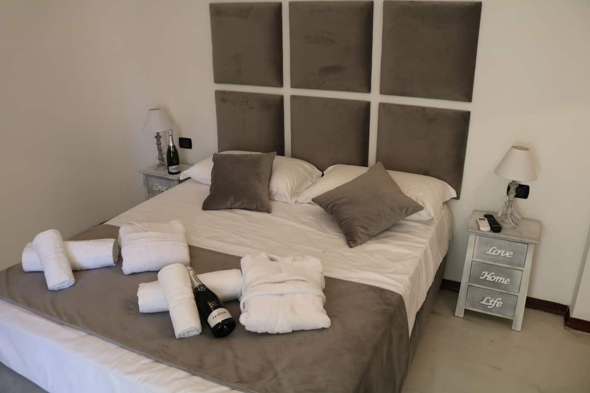 A neatly made bed with a grey headboard, a bedside table with a lamp, and a small drawer with the words "Love," "Home," and "Life" on it.