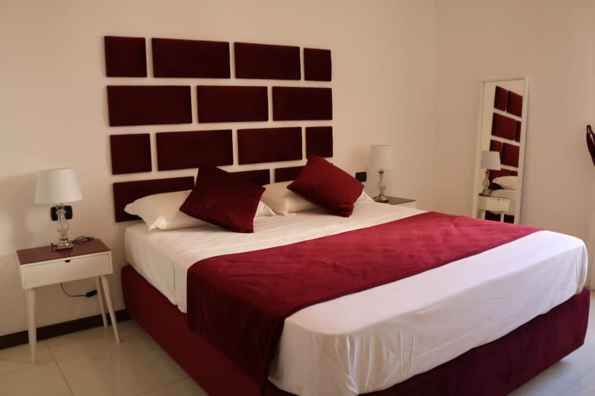 A hotel room with a large bed, a headboard with a geometric pattern, two bedside tables with lamps, and a mirror on the wall.