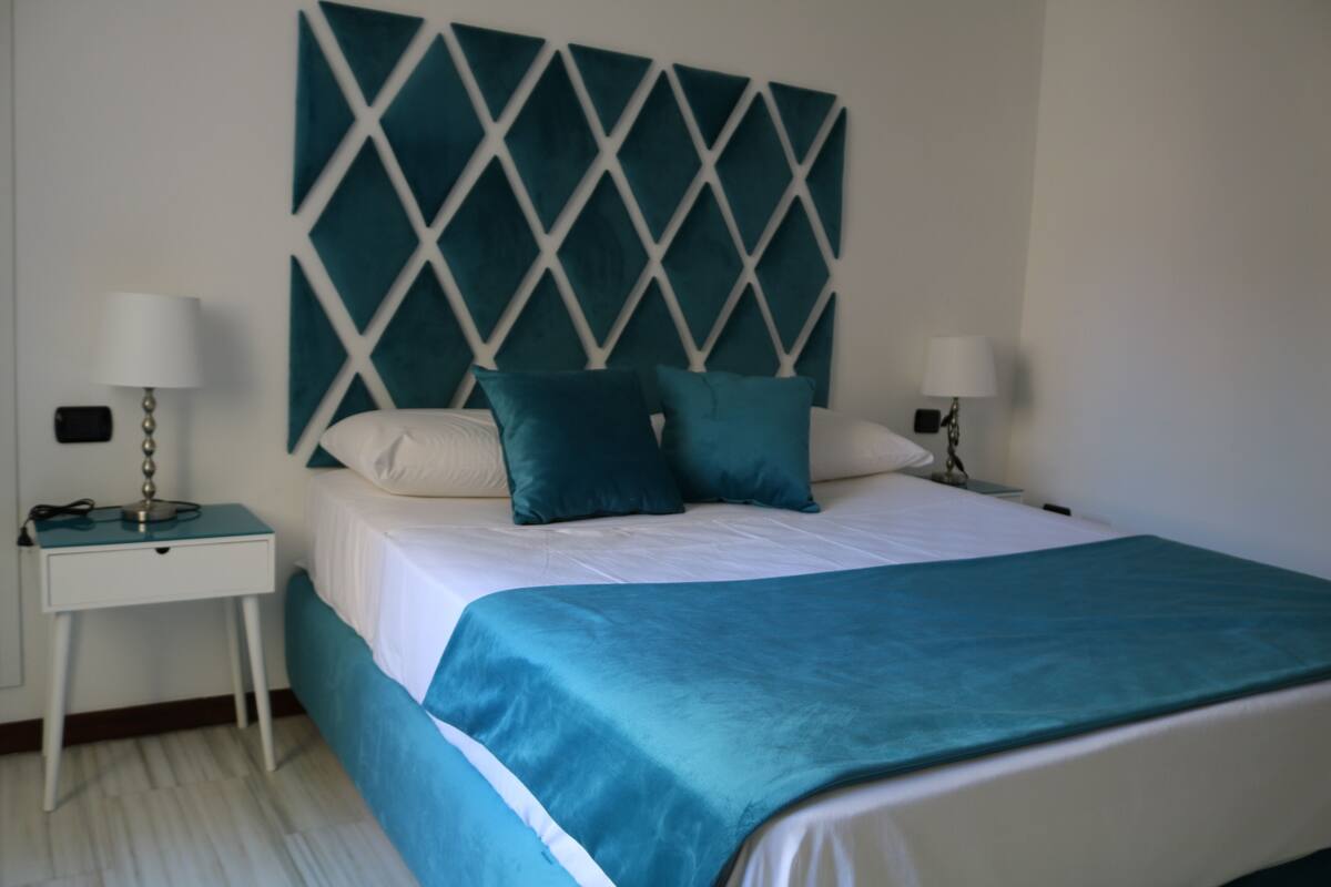 A neatly made bed with a teal headboard, white bedding, and matching teal pillows.