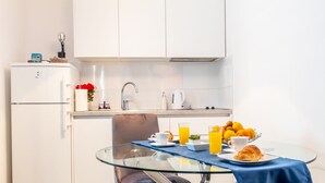A compact kitchen with a glass dining table, a refrigerator, and a coffee maker.