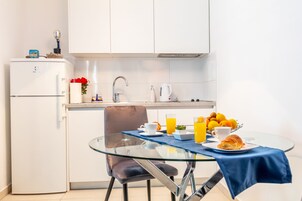 Kompakti keittiö, jossa on lasinen ruokapöytä, jääkaappi ja kahvinkeitin.