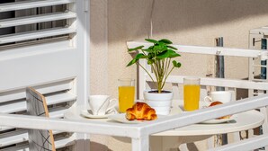 A white metal table with a potted plant, two cups, a glass of orange juice, and a croissant on a balcony.