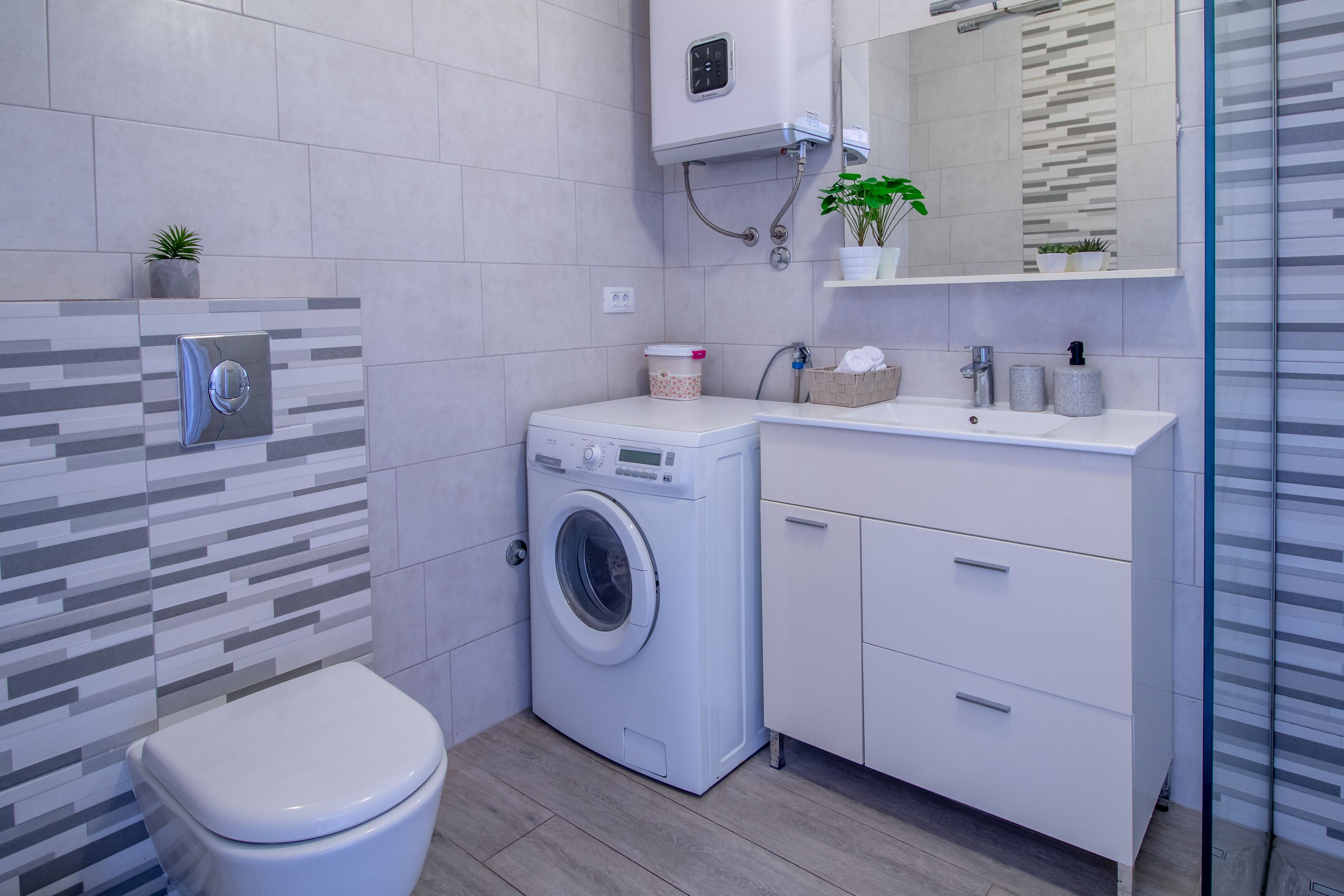 A modern bathroom with a washing machine, toilet, and a glass shower enclosure.