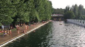 A riverside walkway with people walking and swimming.