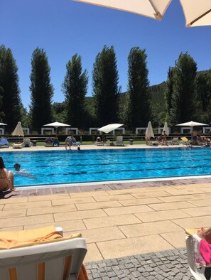 Una piscina con sillas de descanso y sombrillas, rodeada de árboles.