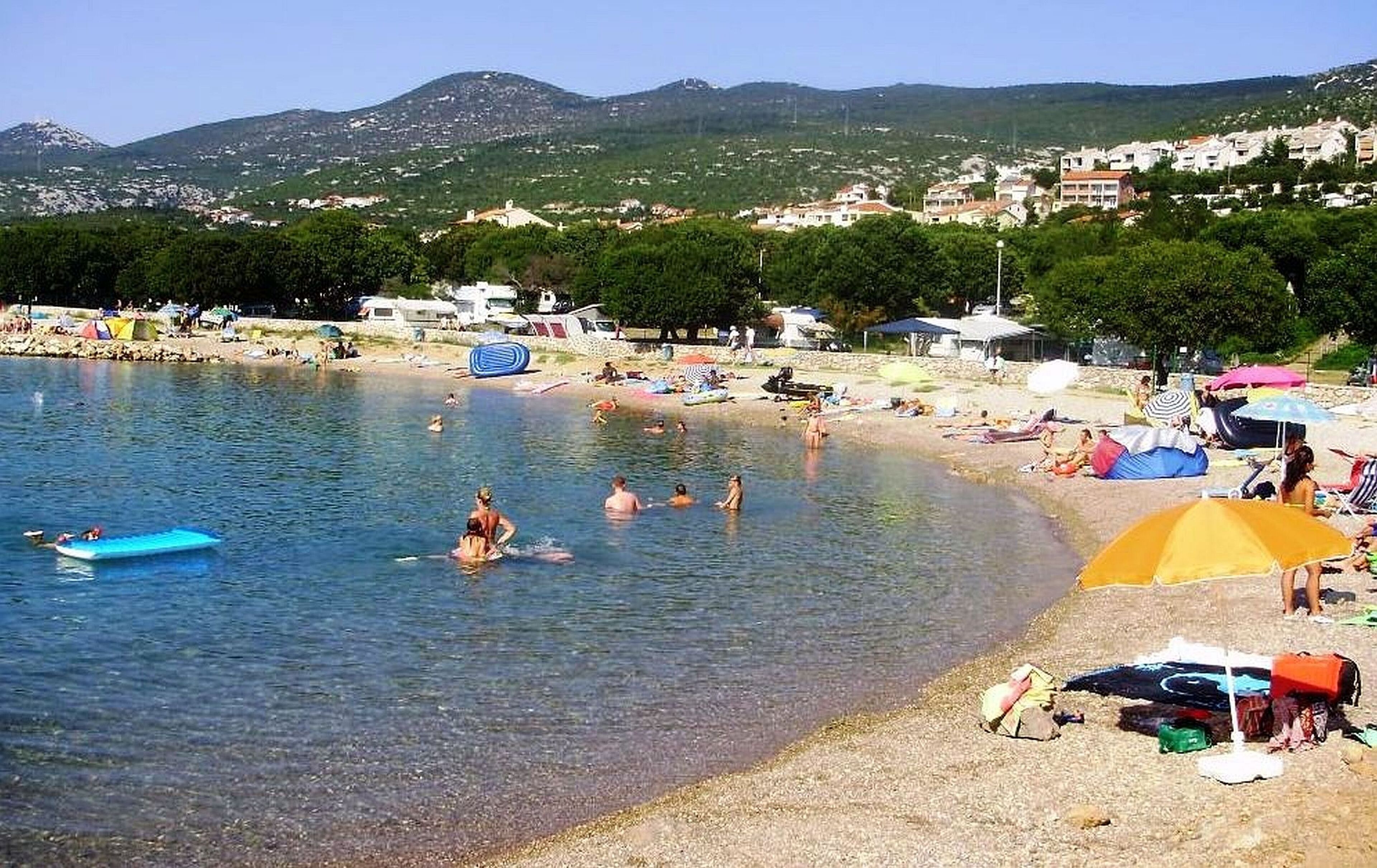 A beach with clear water, people swimming, and beach umbrellas.