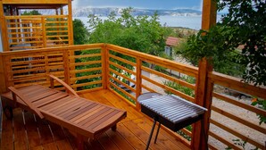 Una terraza de madera con mesa y sillas, con vista a un paisaje pintoresco de montañas y un cuerpo de agua.