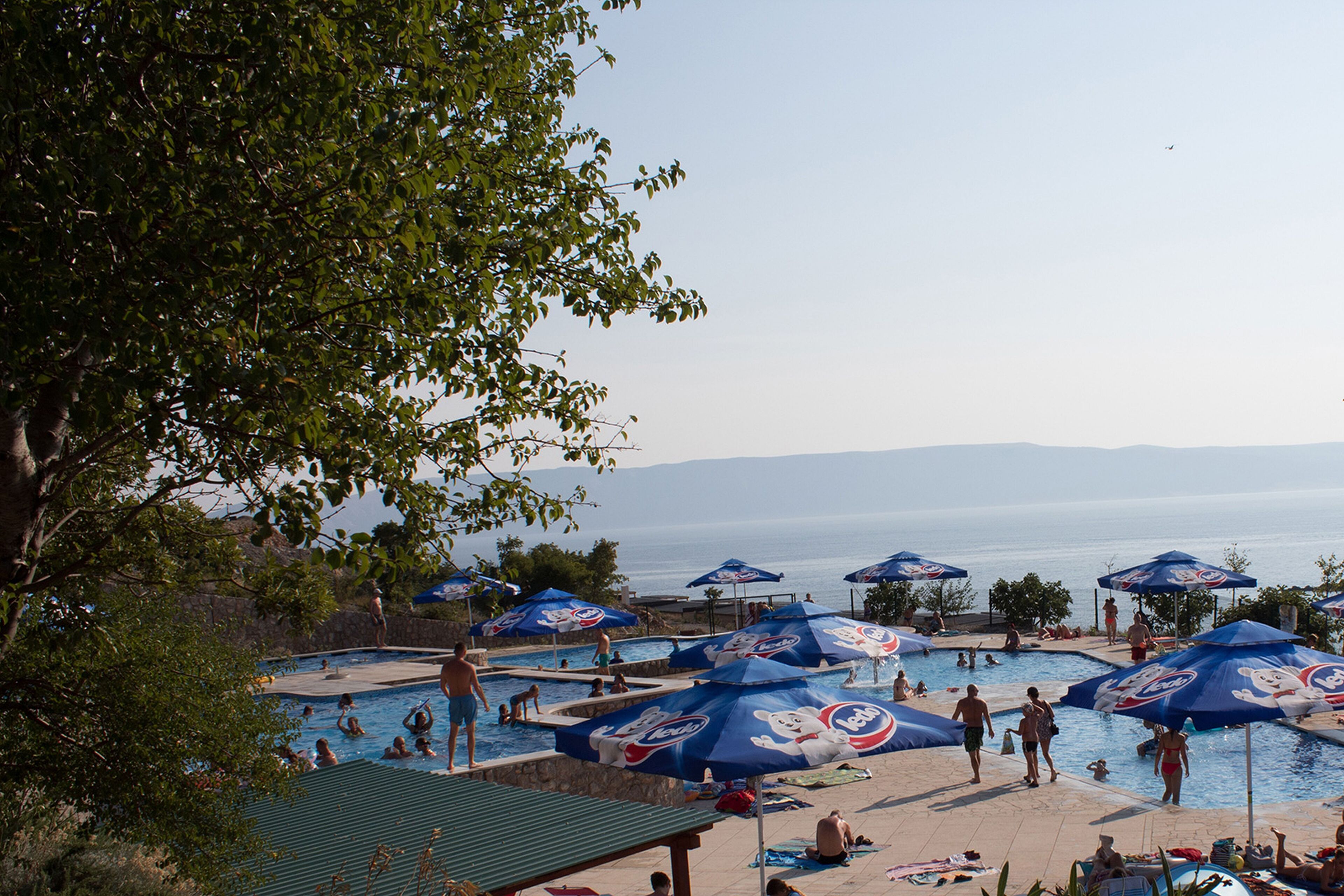 A pool area with multiple umbrellas and people swimming.