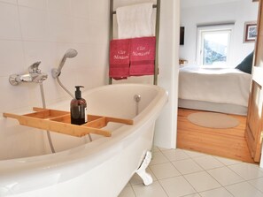Ein Badezimmer mit freistehender Badewanne, einem Holztablett, einer Seifenfiole und einem Handtuchhalter mit roten Handtüchern.