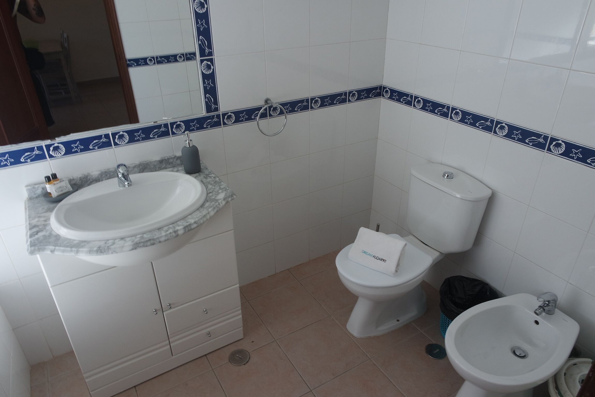 A bathroom with a white sink, toilet, and bidet, a mirror, and a cabinet.
