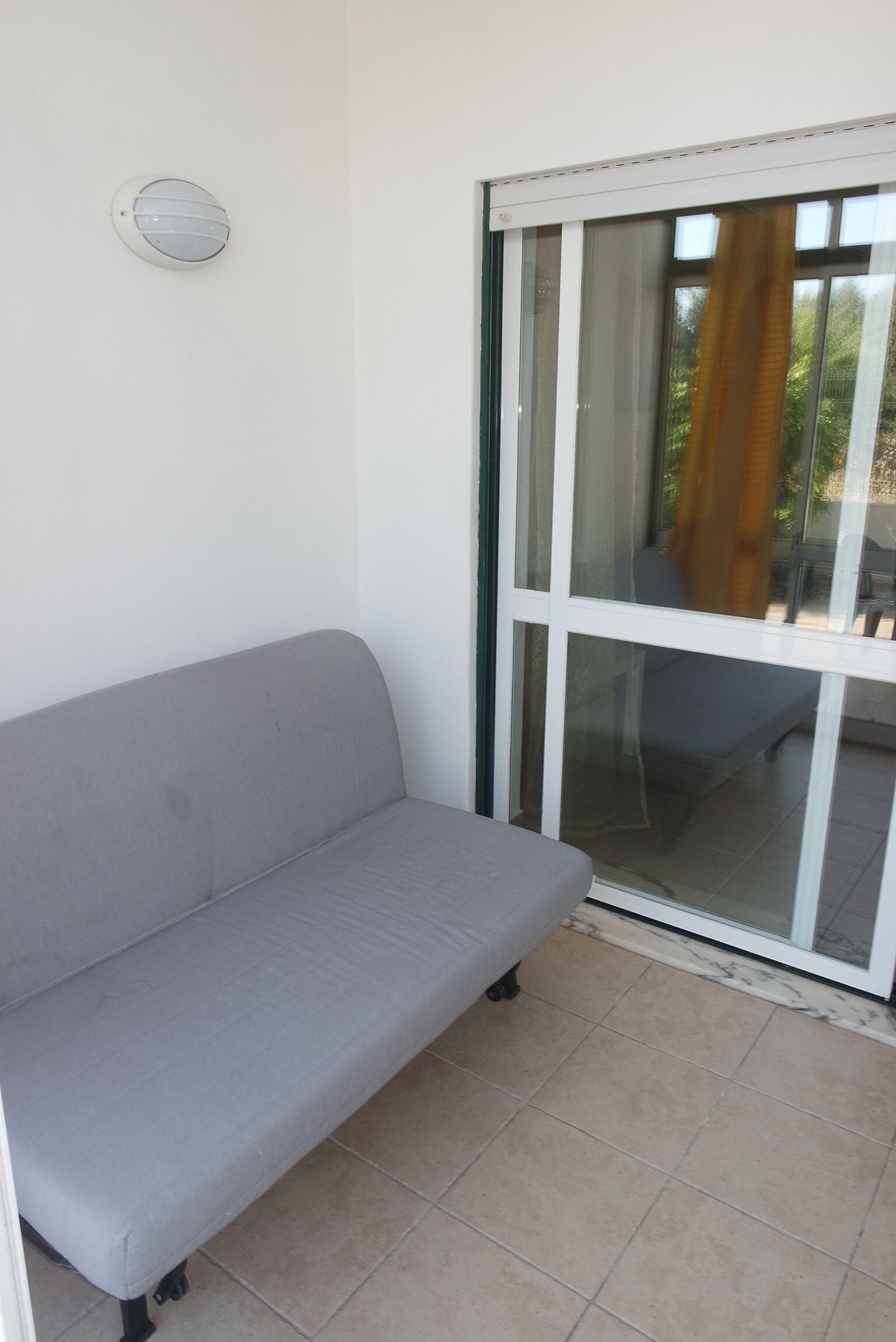 Een grijze bank in een kamer met een schuifdeur naar een buitenruimte.