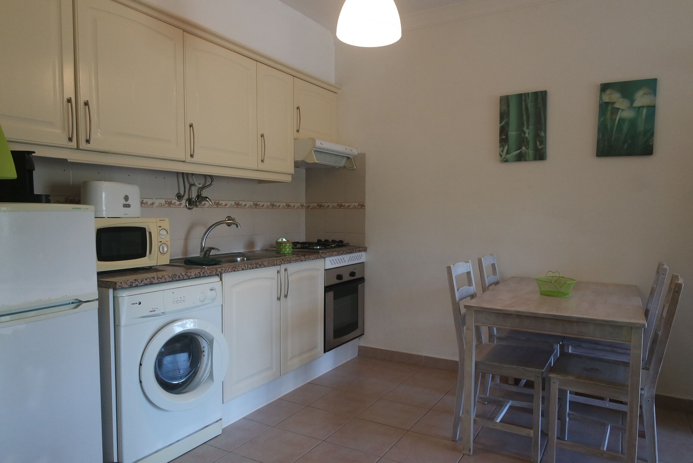 Cocina compacta con lavadora, microondas, estufa y horno. Hay una mesa de comedor con sillas y dos cuadros colgados en la pared.
