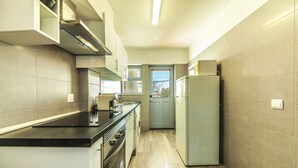 Una cocina compacta con encimera negra, electrodomésticos de acero inoxidable y baldosas de colores claros.
