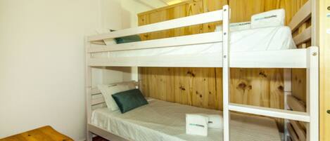 A bunk bed with a wooden headboard, a small wooden table, and a white wall.
