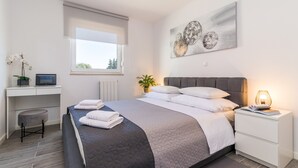 Un dormitorio moderno con una cama grande, un escritorio, una computadora, una planta en maceta y una obra de arte en la pared.