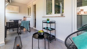 Un balcón con una mesa, sillas y un pequeño estante con plantas.