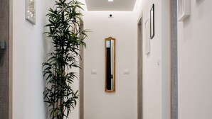 A hallway with patterned tiles, a large potted plant, a mirror, and framed pictures on the walls. - B&B Stramondo (Catania)