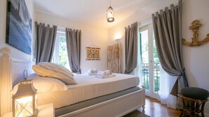 A bedroom with a bed, curtains, a hanging light fixture, a wall-mounted anchor decoration, and a view of greenery outside.