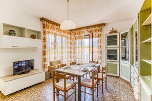 A dining area with a table set for four, surrounded by chairs, a television on a cabinet, and a patterned floor. - Casa Arno 500m from beach (Massa)