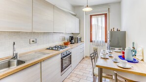 A modern kitchen with a sink, stove, microwave, and oven. There is a dining table with chairs and a window with curtains. - Casa Arno 500m from beach (Massa)