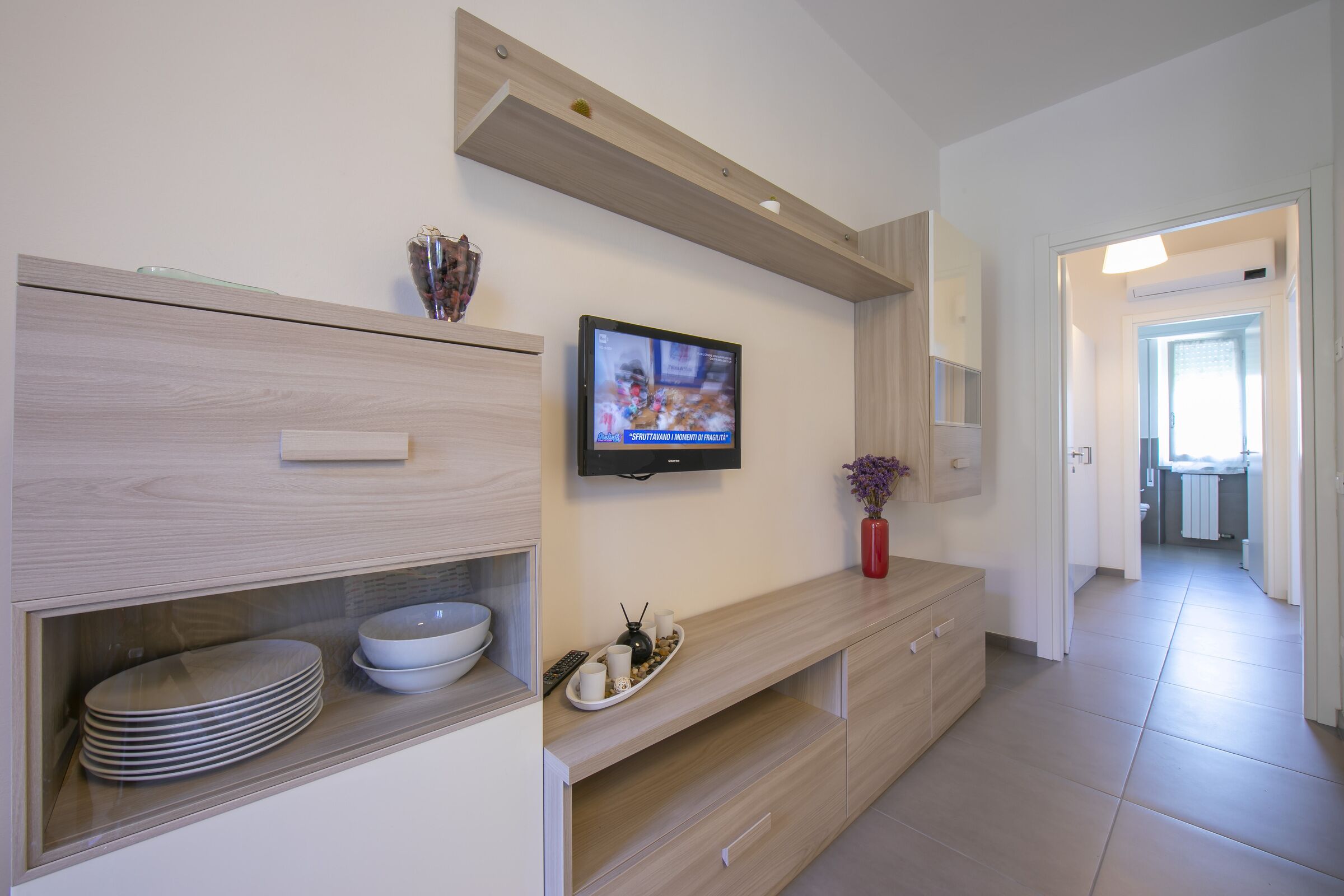 Una cocina moderna con televisor integrado, armarios de madera y un comedor con una bandeja de tazas y platos.