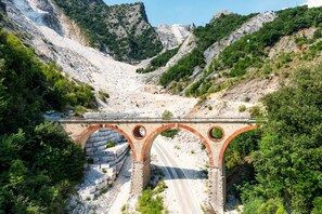 Un puente de piedra con arcos sobre un camino, rodeado de terreno rocoso y vegetación.